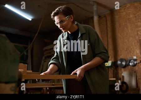 Ein erfahrener Zimmermann konzentriert sich auf die Holzherstellung in einer geschäftigen Werkstatt, umgeben von Werkzeugen und Materialien. Stockfoto