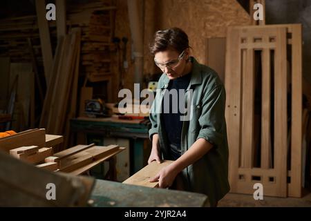 Ein erfahrener Zimmermann arbeitet fleißig mit Holz und formt Materialien in einer einladenden Werkstatt, die mit Werkzeugen gefüllt ist. Stockfoto