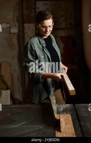 Eine geschickte Frau konzentriert sich intensiv beim Formen von Holz in ihrer gemütlichen Werkstatt, die mit Werkzeugen gefüllt ist. Stockfoto