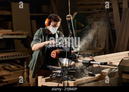 In einer belebten Werkstatt arbeitet eine geschickte Tischlerin fleißig mit einer Motorsäge, um Holzstücke zu Formen. Stockfoto