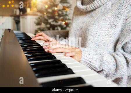 Frau, die zu Hause elektrisches Klavier spielt, während der Weihnachtsferien. Nahaufnahme der weiblichen Hände auf den Klaviertasten. Stockfoto