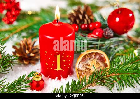 Bayern, Deutschland - 11. November 2024: Rote Adventskerze mit der Nummer 1 brennt in einer festlichen Adventsarrangements, umgeben von Tannenzweigen, Beeren und getrockneten Orangenscheiben. Erster Advent. *** Rote Adventskerze mit der Zahl 1 brennt im festlichen Adventsgesteck, umgeben von Tannenzweigen, Beeren und getrockneten Orangenscheiben. Erste Adventszeit. Stockfoto