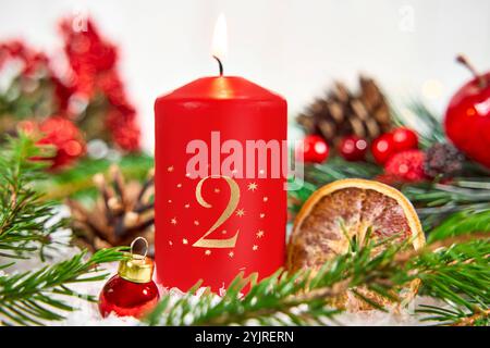 Bayern, Deutschland - 11. November 2024: Rote Adventskerze mit der Zahl 2 brennt in einer festlichen Adventsarrangements, umgeben von Tannenzweigen, Beeren und getrockneten Orangenscheiben. Zweiter Advent. *** Rote Adventskerze mit der Zahl 2 brennt im festlichen Adventsgesteck, umgeben von Tannenzweigen, Beeren und getrockneten Orangenscheiben. Zweiter Advent. Stockfoto