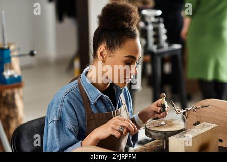 Eine geschickte Frau entwirft sorgfältig komplizierten Schmuck und konzentriert sich dabei intensiv auf ihren Arbeitsplatz. Stockfoto