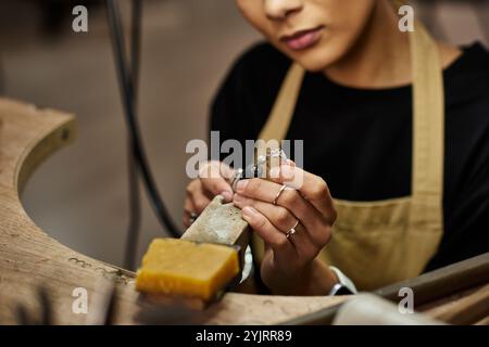 Eine talentierte Frau konzentriert sich intensiv, wenn sie mit Präzisionswerkzeugen exquisite Schmuckstücke formt. Stockfoto