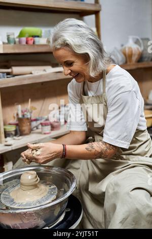 Eine geschickte reife Frau formt in ihrem Atelier freudig Ton auf einem Keramikrad. Stockfoto