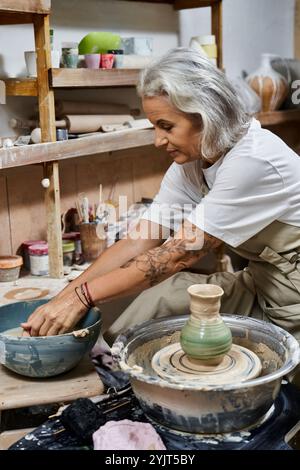 Eine geschickte Frau formt Ton auf einem Töpferrad, umgeben von Werkzeugen und künstlerischen Kreationen. Stockfoto