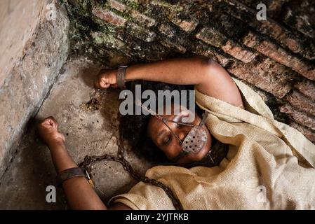 Porträt einer schwarzen Frau, gekettet und mit einer eisernen Maske über dem Mund, die auf dem Boden liegt. Sklaverei in Brasilien. Darstellung der Sklavin Anastacia. Stockfoto