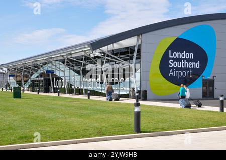 Flughafen London Southend. Passagiere mit Gepäck, die in Richtung des Terminalgebäudes fahren, mit dem London Southend Airport Logo und dem Symbol Stockfoto