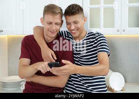 Glückliche Brüder, die in der Küche auf das Smartphone schauen Stockfoto