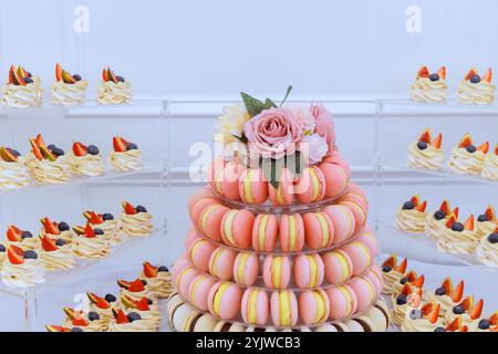 Das atemberaubende Dessert-Arrangement zeigt einen hohen Macaron-Turm in verschiedenen Farben, umgeben von kleinen Backwaren mit Früchten. Stockfoto