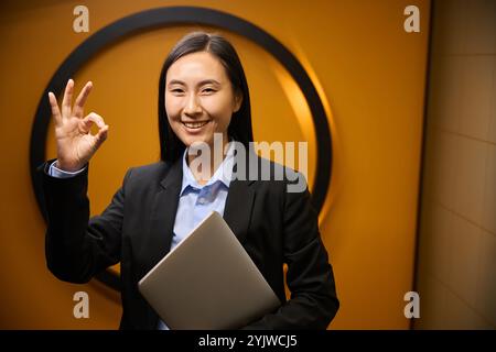 Schöne asiatische Frau in dunkler Jacke vor dekorativer Wand Stockfoto