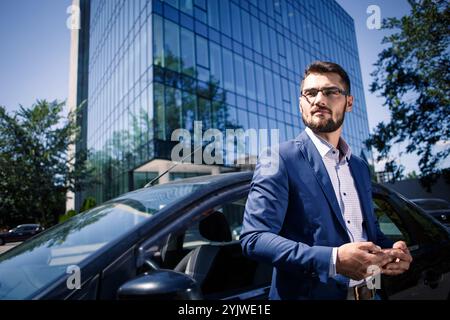 Junger Geschäftsmann, der neben dem Auto steht und das Telefon hält Stockfoto