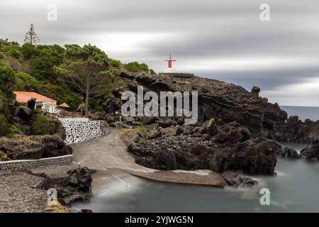 Die Windmühle von Urzelina, Sao Jorge Island, Azoren, befindet sich neben dem kleinen Hafen mit Schwimmbereich. Stockfoto