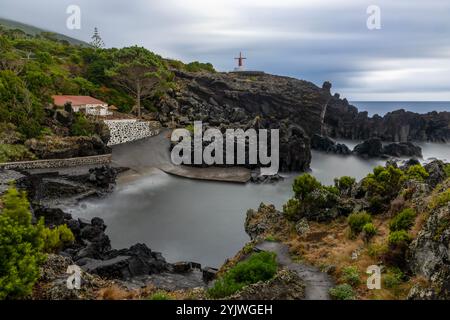 Die Windmühle von Urzelina, Sao Jorge Island, Azoren, befindet sich neben dem kleinen Hafen mit Schwimmbereich. Stockfoto