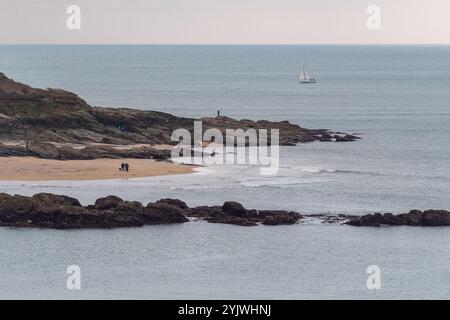 Blick auf East Portlemouth, Limebury Point, mit Wanderern am Strand, einem einsamen Fischer mit Rute und einer Yacht mit Felsen im Vordergrund - Frühlingstag. Stockfoto