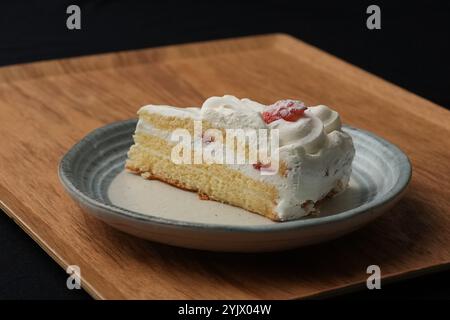 Ein kleiner japanischer Erdbeerkuchen auf einem stilvollen japanischen Teller auf einem Holztablett auf einem schwarzen Tuch auf einem weißen Tisch. Stockfoto
