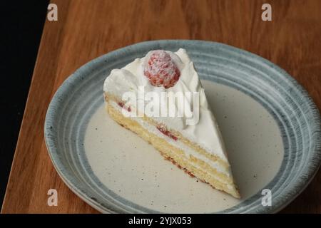 Ein kleiner japanischer Erdbeerkuchen auf einem stilvollen japanischen Teller auf einem Holztablett auf einem schwarzen Tuch auf einem weißen Tisch. Stockfoto