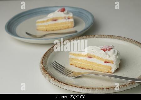 Japanischer Erdbeer-Shortcake und Gabel auf jedem stilvollen großen und kleinen Teller auf einem weißen Tisch. Stockfoto