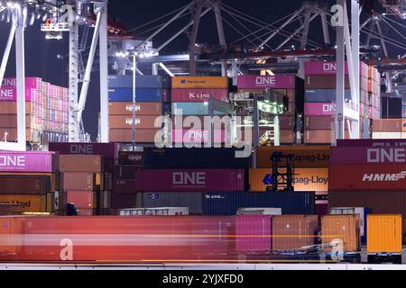 Wilmington, Kalifornien, USA - 16. Juli 2021: Kräne entladen intermodale Container von einem Schiff im Hafen von Los Angeles, während Sattelzüge transportieren Stockfoto