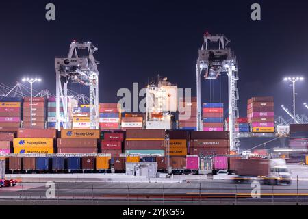 Wilmington, Kalifornien, USA - 16. Juli 2021: Kräne entladen intermodale Container von einem Schiff im Hafen von Los Angeles, während Sattelzüge transportieren Stockfoto