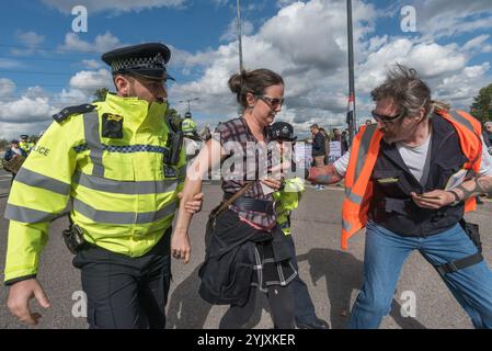 London, Großbritannien. 9. September 2017 die Polizei führte eine Frau fort, die verhaftet wurde, weil sie auf der Straße auf dem Festival of Resistance Against DSEI Arms Fair saß, um Lastkraftwagen mit Waffen zu blockieren. Die Defence & Security Equipment International, die von der britischen Regierung unterstützt wird, ist der Ort, an dem Rüstungsunternehmen und Waffenhändler Waffen an Länder auf der ganzen Welt verkaufen, einschließlich vieler repressiver Regime. Die Straße am Osttor wurde von zwei Demonstranten durch eine Schleuse blockiert, und andere, darunter diese Gruppe, saßen auf der Straße davor, wobei eine große Gruppe ein Quäker-Treffen abhielt. Die Polizei versuchte, die Straße freizumachen und machte mehrere Stockfoto