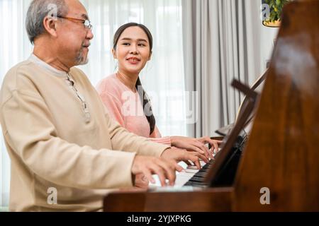 Glückliche Tochter und älterer Vater, die zusammen im Wohnzimmer Musik auf dem Klavier spielen Stockfoto
