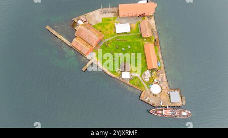 Aus der Vogelperspektive auf eine kleine Insel mit Gebäuden, grünem Gras und einem vom Wasser umgebenen Boot. Stockfoto