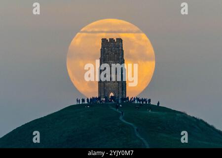 Glastonbury, Somerset, Großbritannien. November 2024. Wetter in Großbritannien. Der volle Bibermond steigt in den klaren Nachmittagshimmel hinter dem St. Michael’s Tower am Glastonbury Tor in Somerset auf, während sich eine Menschenmenge auf dem Hügel versammelt, um zu beobachten. Dieser Monat voller Bibermond ist der letzte Supermond des Jahres. Bildnachweis: Graham Hunt/Alamy Live News Stockfoto