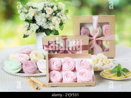 Buntes hausgemachtes zephyr oder Marshmallows in der Box auf einem weißen Tisch mit einem Blumenstrauß Stockfoto