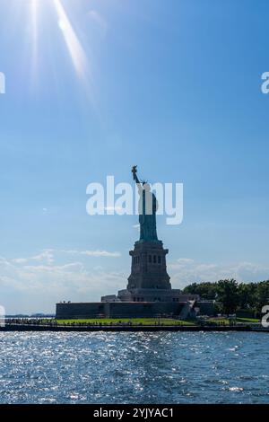 New York City, USA - 20. August 2022: Blick auf Liberty Island und Freiheitsstatue vom Wasser mit Sonnenstrahl, New York City, USA. Stockfoto