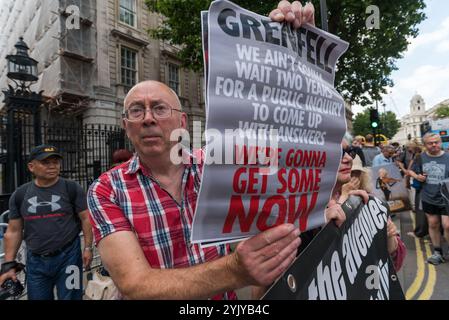 London, Großbritannien. Juni 2017. Ian Bone of Class war steht hinter ihrem Banner vor der Downing Street gegenüber dem großen Protest, der Theresa May zum Rücktritt aufruft. Er hält ein Poster hoch: "Grenfell - Wir werden nicht zwei Jahre warten, bis eine öffentliche Anfrage Antworten gibt - wir werden JETZT welche holen". Stockfoto