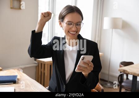 Glückliche Geschäftsfrau, die ihr Smartphone hält, feiert tolle unglaubliche Neuigkeiten Stockfoto