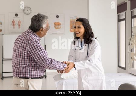 Lächelnder Arzt in weißem medizinischem Mantel grüßt älteren männlichen Patienten Stockfoto