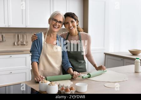 Mutter und Tochter tragen Schürzen, die in der Küche posieren Stockfoto
