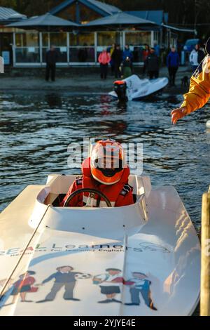 Ein Motorboot-Racer legt sein Boot an und eine Person greift zu ihm, um ihm während der Coniston Power Boat Records Week auf dem Steg/Dock auf Coniston Water zu helfen. Stockfoto