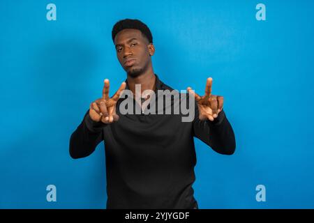Porträt eines jungen Mannes mit Friedenszeichen mit beiden Händen auf blauem Hintergrund Stockfoto