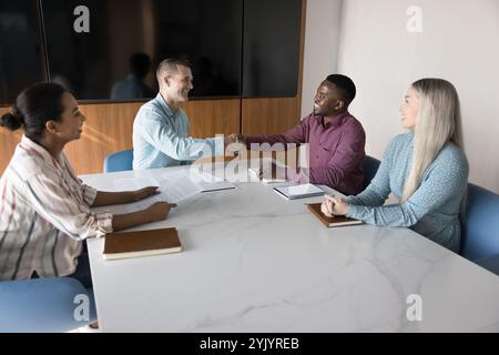 Selbstbewusster positiver Unternehmensleiter, der männlichen afrikanischen Angestellten die Hand schüttelt Stockfoto