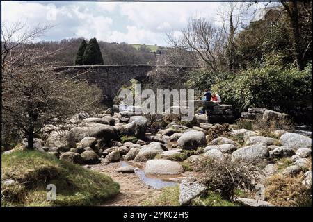 Clapper Bridge, Dartmeet, Widecombe im Moor, Teignbridge, Devon, 1979. Ein Blick aus dem Nordosten einer Gruppe, die auf den Überresten der Clapper Bridge sitzt, nördlich der Dartmeet Bridge. Stockfoto