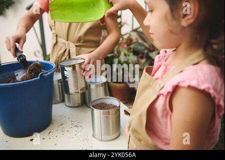 Kleine Kinder, die im Garten arbeiten und Blechdosen mit Boden füllen. Förderung von Kreativität und Nachhaltigkeit durch praxisnahe Naturprojekte Stockfoto