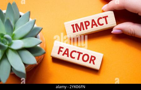 Symbol für Aufprallfaktor. Holzblöcke mit den Worten Impact Factor. Schöner oranger Hintergrund mit saftiger Pflanze. Geschäftsmann Hand. Business und Impact Stockfoto