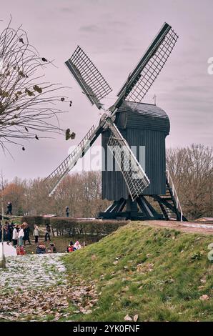 Ein Winterblick auf die historische nachgebildete Windmühle auf dem Burggraben Bourtange mit Lichtern und vorbeischlendernden Besuchern des Weihnachtsmarktes. Stockfoto