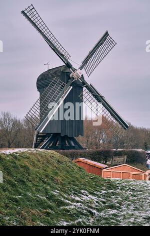 Ein Winterblick auf die historische nachgebildete Windmühle auf dem Burggraben Bourtange mit Lichtern und Weihnachtsmarkt-Besuchern im Hintergrund Stockfoto