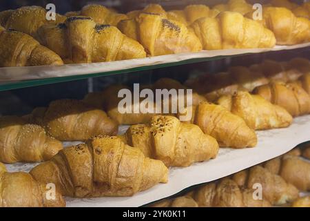 Viele frisch gebackene französische Croissants auf einem Regal in einer Bäckerei. Frisches klassisches Gebäck zum Frühstück und Kaffee. Herstellung von Backwaren Stockfoto