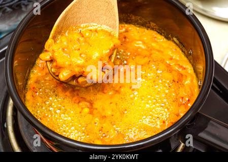 Kochende Sanddornbeeren mit Kristallzucker in einem Topf mit einem Holzlöffel rühren. Hausmannskost. Stockfoto