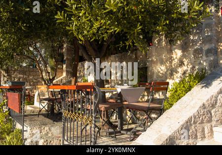 Ein einladender Outdoor-Speisesaal mit rustikalem Charme, umgeben von Steinmauern und strahlendem Sonnenlicht, perfekt für ein gemütliches, friedliches Essen in der Natur. Stockfoto