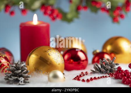 Rote und goldene Weihnachtskugeln neben einer beleuchteten Kerze auf künstlichem Schnee, dekorative festliche Atmosphäre Stockfoto