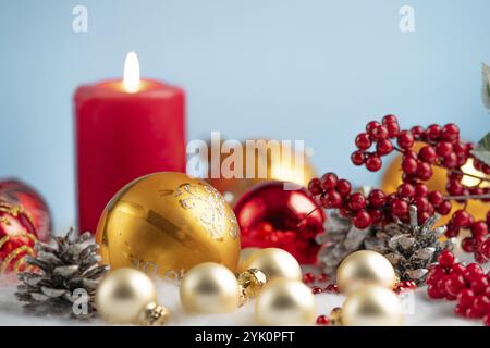 Weihnachtsdekoration mit roten und goldenen Kugeln, einer brennenden Kerze und Tannenzapfen auf blauem Hintergrund Stockfoto