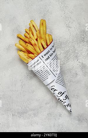 Frittierte Pommes frites in einer Papiertüte, auf abstraktem Hintergrund, ohne Menschen, im rustikalen Stil, in einer Kegelpackung, Zeitung, einer Tüte aus der Zeitung Stockfoto