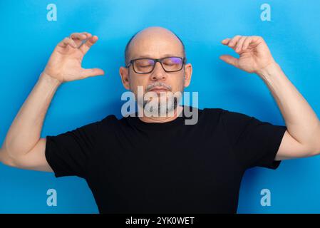 Bärtiger, kahler Mann, der eine Brille trägt und ein schwarzes Hemd, der mit den Armen zur Kamera geht. Selbstbewusst und ruhig. Studio-Aufnahme. Stockfoto